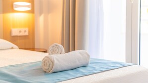 A hotel room with a neatly made bed, a blue bedspread, and a rolled white towel on the bed.