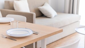 A dining table with plates, cutlery, and a glass, set in a modern living room with a sofa and a small round table.