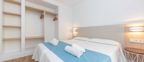 Habitación de hotel con cama, toalla azul, suelo de madera y armario blanco con espacio para colgar.