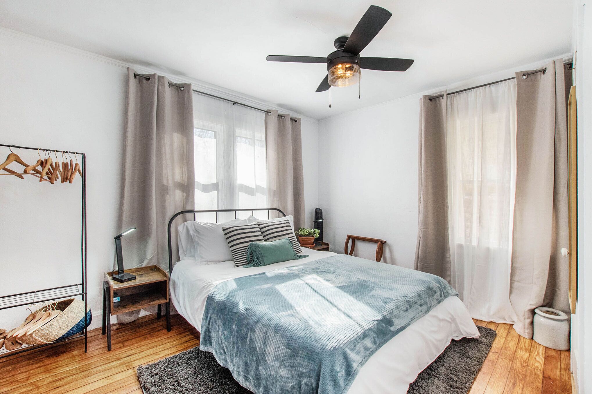 A bedroom with a bed, a bedside table, a nightstand, a ceiling fan, and a window with curtains.