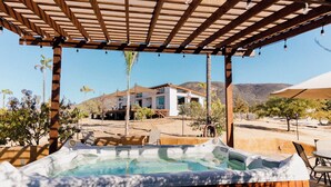 Un bain à remous sous une pergola en bois, avec vue sur une maison moderne et, au loin, sur des montagnes.