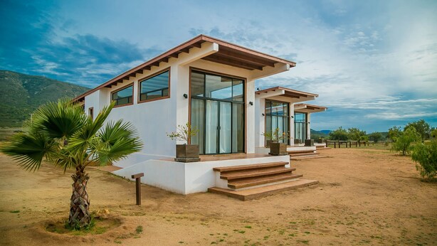 Une maison moderne à deux étages, dotée de grandes fenêtres et d’un porche en bois.