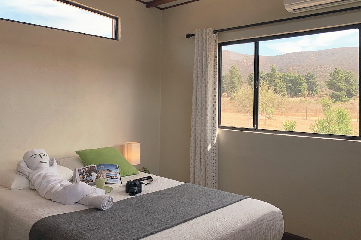 A hotel room with a bed, a lamp, a camera, and a view of a desert landscape.