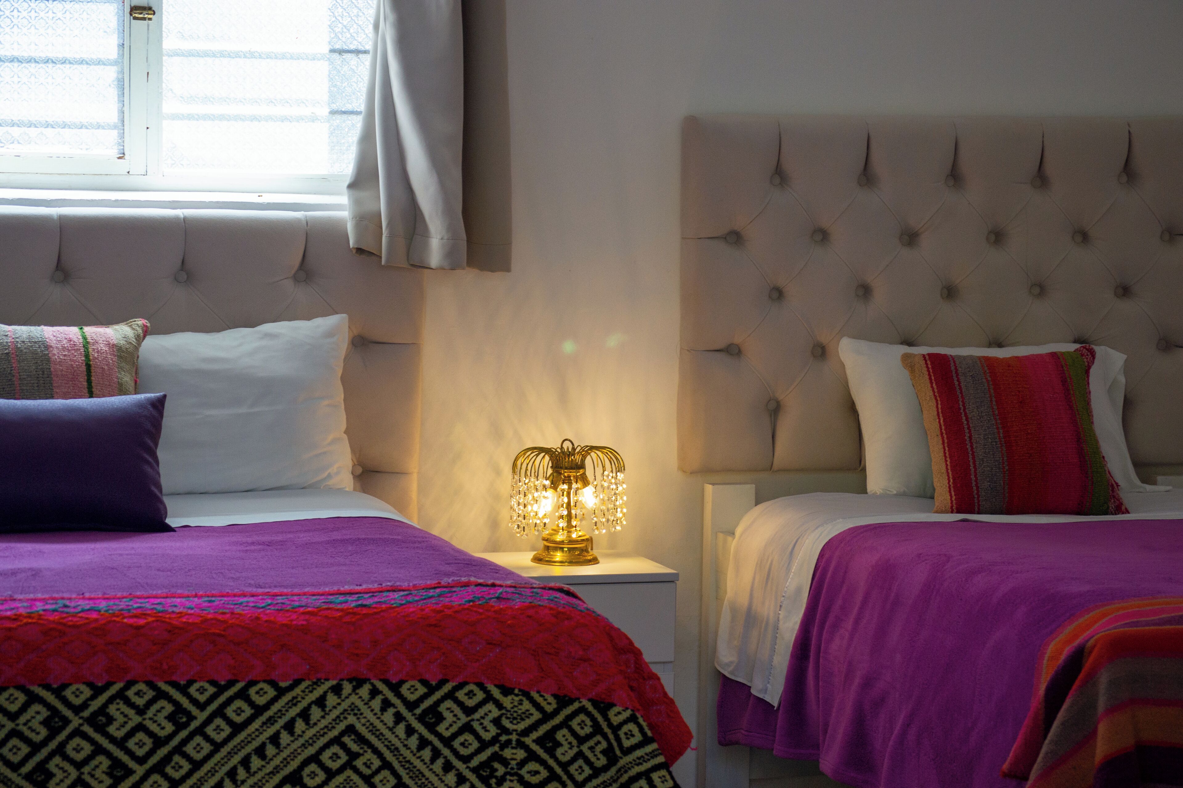 Ein Hotelzimmer mit zwei Betten, jedes mit einem eigenen Kopfteil und Kissen, und einem Nachttisch mit einer Lampe dazwischen.