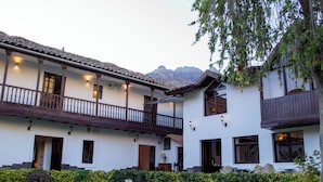 Un edificio a due piani con un balcone, un giardino curato e montagne sullo sfondo.