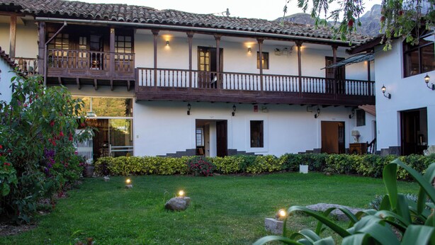 Un edificio a due piani con un balcone, un giardino con prato e un siepe curata.