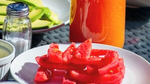 Un tavolo con una caraffa di succo d'arancia, un piatto di anguria e una ciotola di avocado a fette.