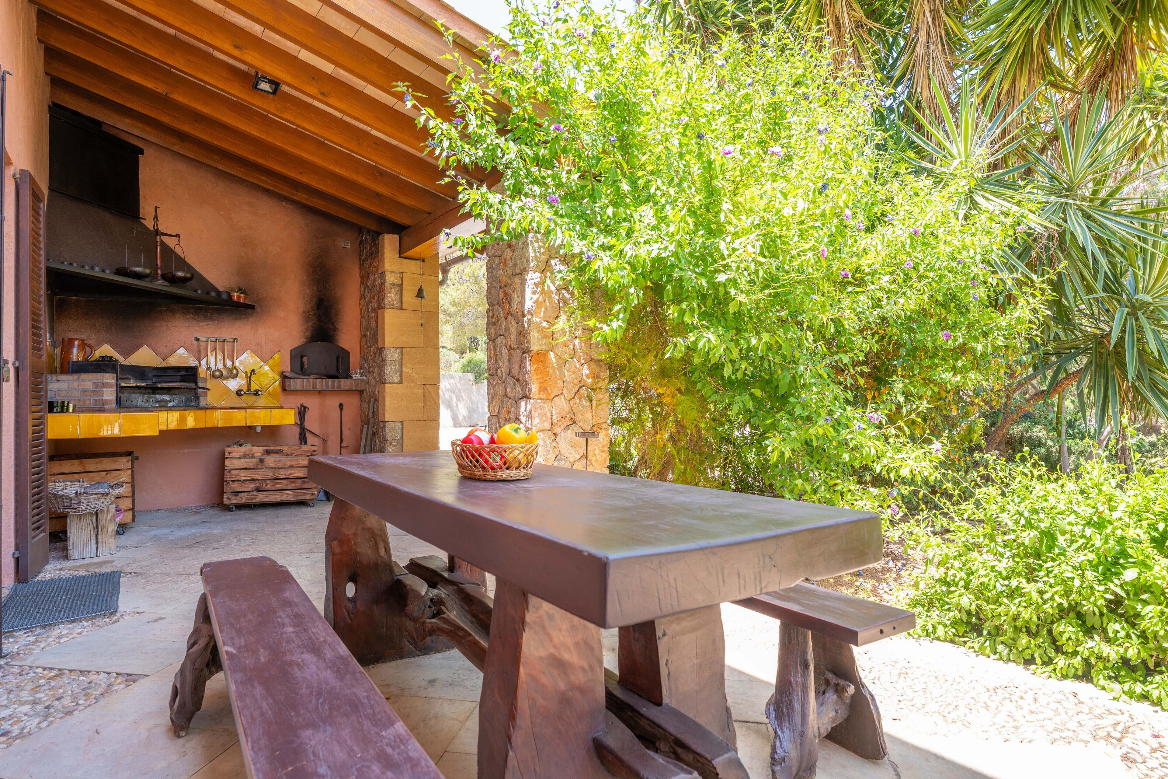 Un espace cuisine extérieur avec un mur en pierre, une table en bois et des bancs.