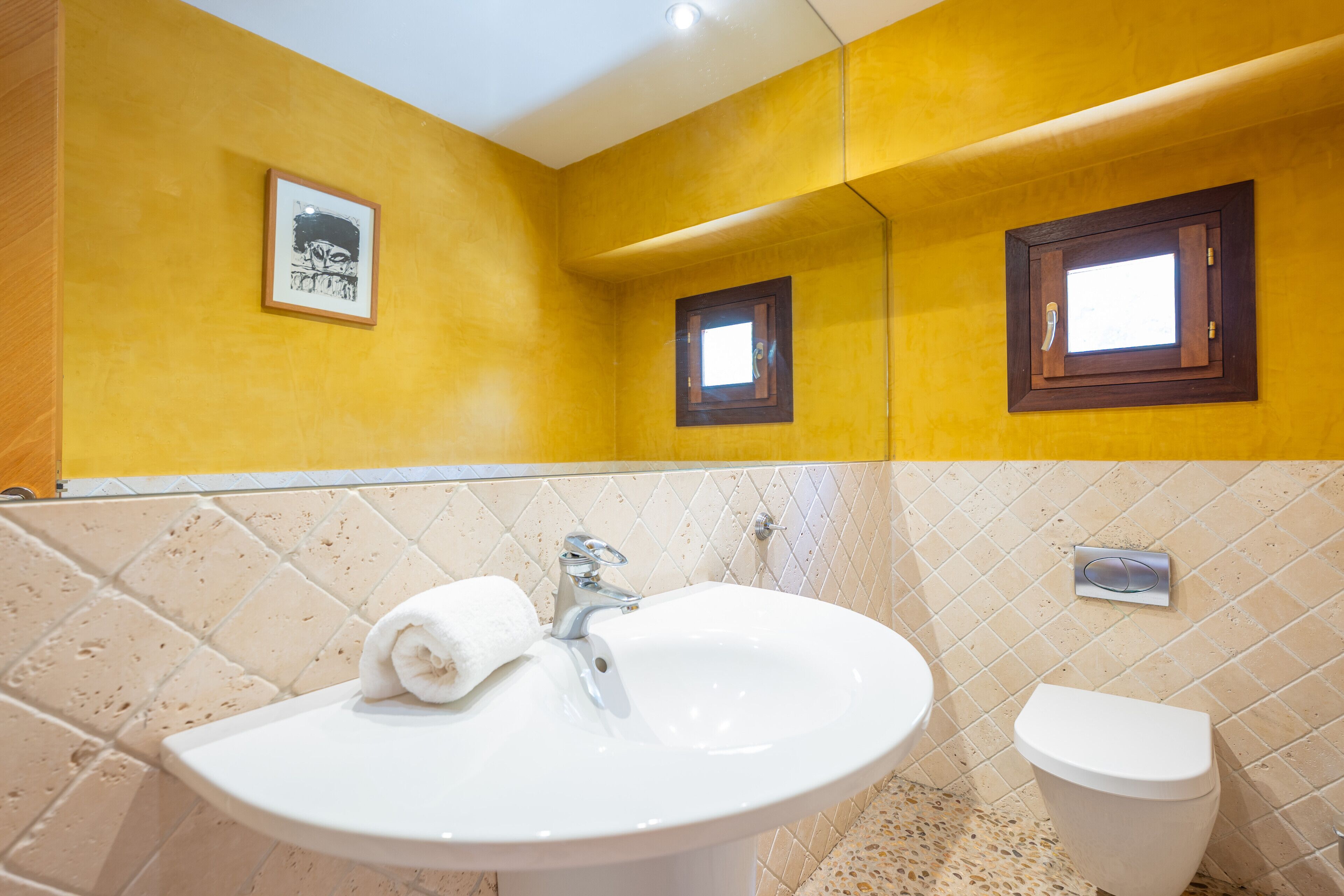 Une salle de bain avec un lavabo, des toilettes et deux petites fenêtres.