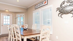 A dining area with a wooden table and white chairs, a sign above the table, and a decorative crab on the wall.