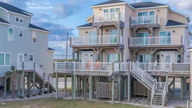 A multi-story beachfront property with balconies, a covered deck, and a staircase leading to the entrance.
