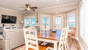 A spacious living area with a wooden dining table, white chairs, a ceiling fan, and a television. - Crab House - Oceanfront 5 BR Home with Hot Tub & Community Pool (North Topsail Beach)