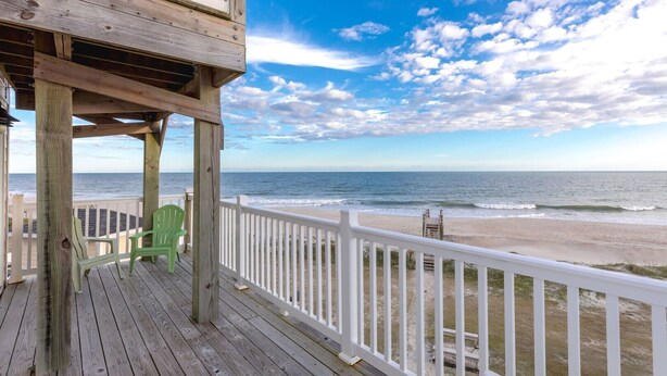 A wooden deck with a white railing, a green chair, and a view of the beach and ocean. - Crab House - Oceanfront 5 BR Home with Hot Tub & Community Pool (North Topsail Beach)