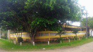 Um edifício com fachada amarela, cercado por uma vedação e árvores.