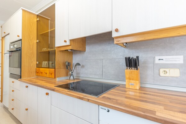 Una cocina moderna con armarios blancos, encimera de madera, horno empotrado y un bloque para cuchillos.