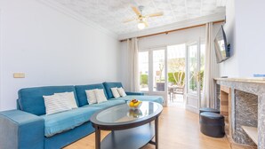 A living room with a blue sofa, a glass coffee table, a ceiling fan, and a fireplace. - CAN MIQUEL (TORD) - Fantastic house with terrace and private pool, and located just 300 me (Muro)