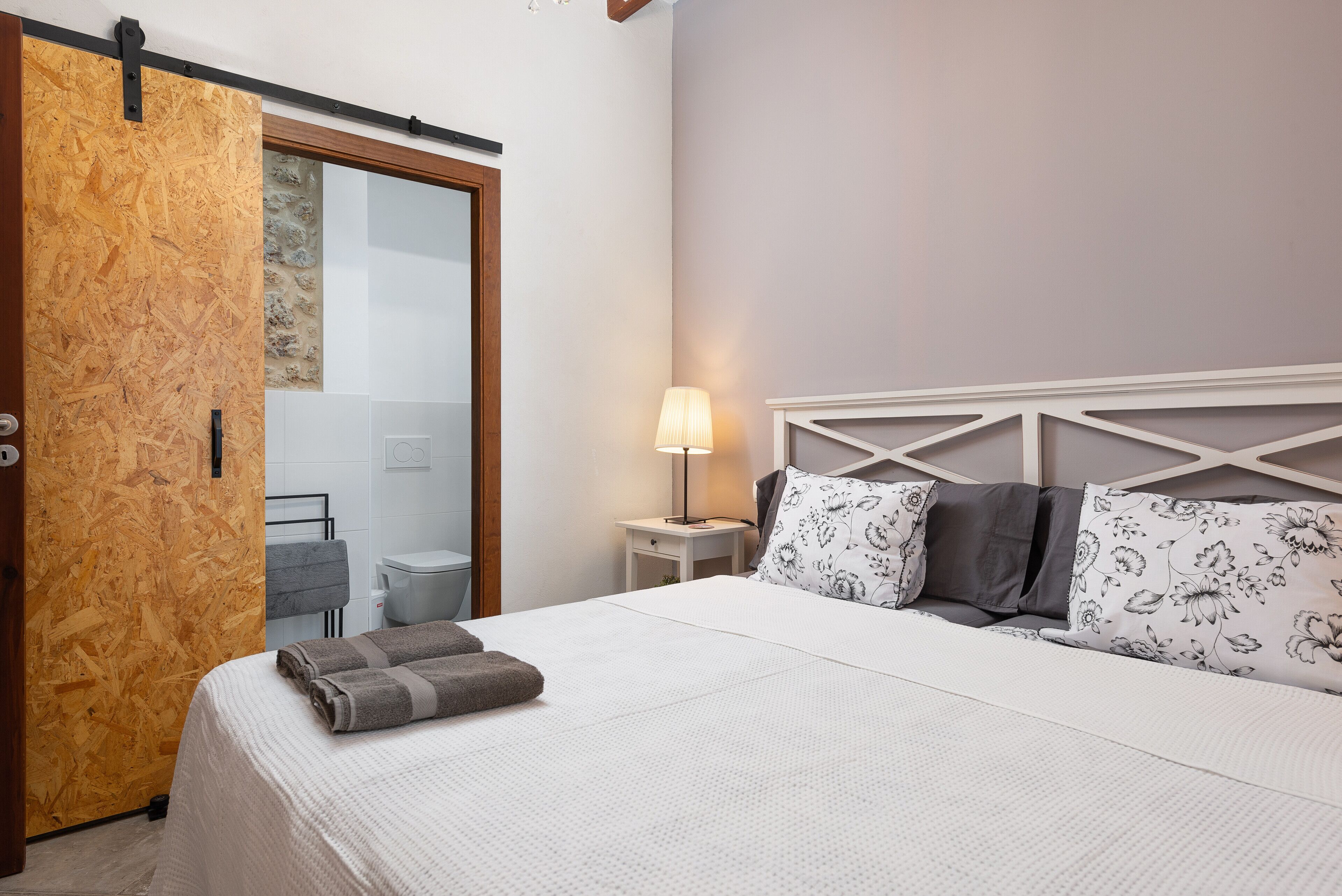 A bedroom with a bed, a nightstand, a lamp, and a sliding door.