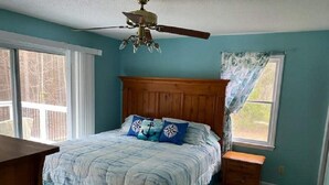 Un dormitorio con cabecera de madera, cama con ropa de cama azul, mesita de noche y ventilador de techo.