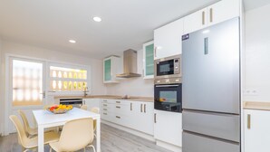 A modern kitchen with white cabinets, a stainless steel refrigerator, a microwave, and a dining area with a table and chairs. - PDM CA'N NOFRE - Fantastic cosy house with terrace and with a the beach just 230 metres aw (Muro)