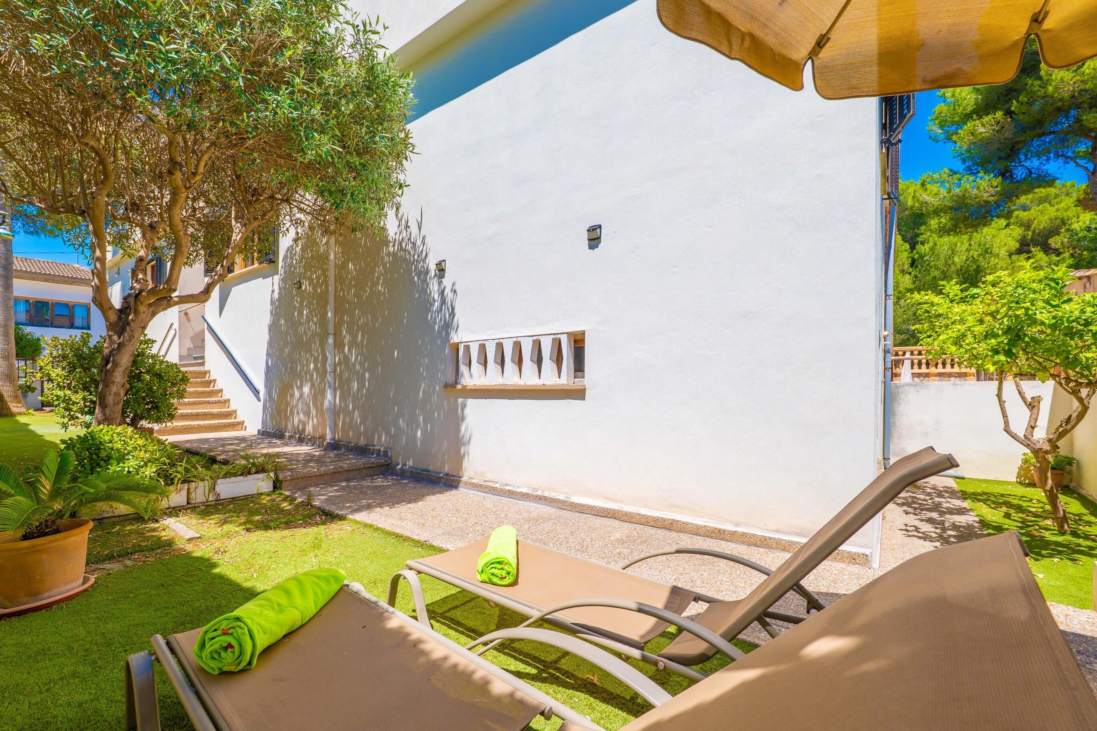 Eine Terrasse mit Tisch und Stühlen, ein kleiner Garten und ein weißes Gebäude mit Fenster und Tür.
