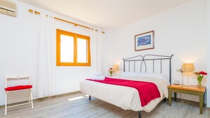 A bedroom with a bed, a chair, a bedside table, a lamp, and a window. - PDM CA'N NOFRE - Fantastic cosy house with terrace and with a the beach just 230 metres aw (Muro)