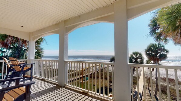 A covered outdoor area with a view of the ocean, featuring a wooden deck and white railings.