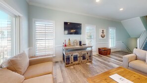 Un amplio salón con una mesa de centro de madera, sofás color beige y un televisor montado en la pared.