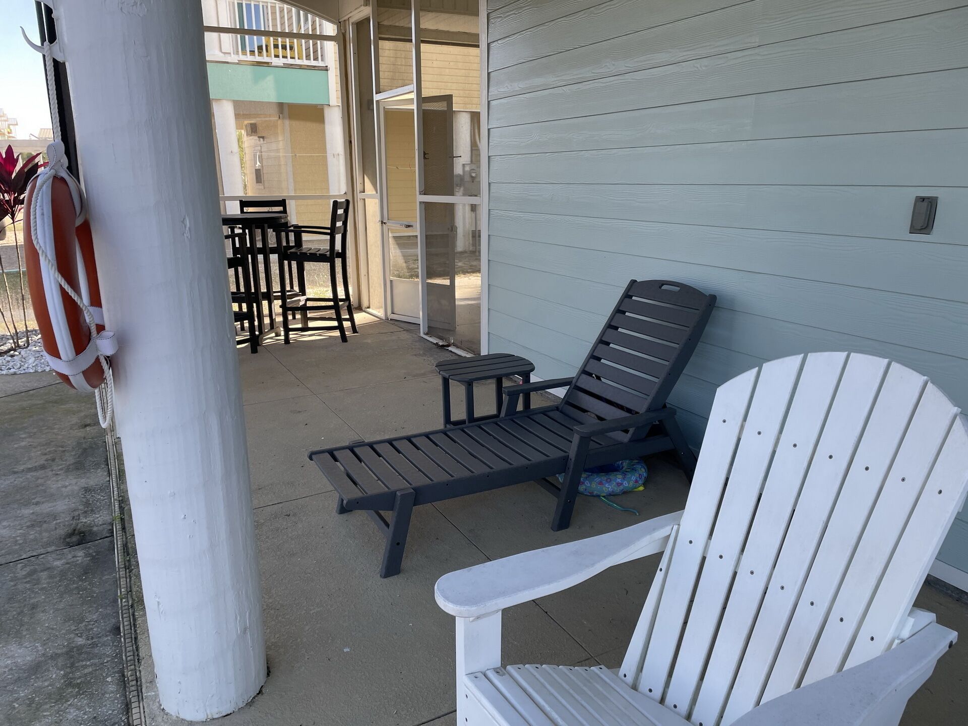 Een overdekt terras met twee loungestoelen, een bijzettafeltje en een bank.