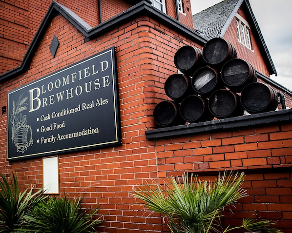 Un edificio de ladrillo con un letrero que anuncia 'Bloomfield Brewhouse', ofreciendo cervezas de barril, buena comida y alojamiento familiar.