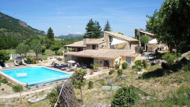 Een villa met zwembad, terras en een bergachtig landschap op de achtergrond.