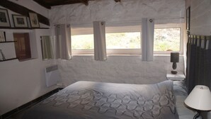 Een slaapkamer met een bed, nachtkastje, lamp, raam met gordijnen, een wandheater en lijstjes met foto's aan de muur.
