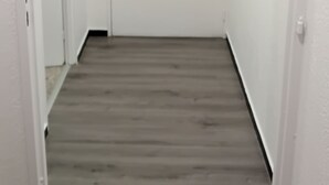 Kapea käytävä, jossa on puulattia ja joka johtaa valkoisiin oviin.