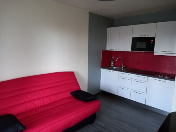 Eine kleine Küche mit weißen Schränken, einer roten Arbeitsplatte und einem roten Sofa mit schwarzen Kissen.