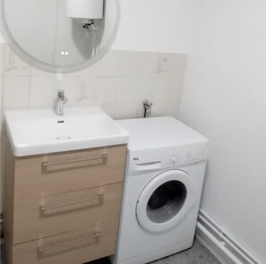 Ein kleines Badezimmer mit einem weißen Waschbecken, einem Holzkasten und einer Waschmaschine mit Frontlader.