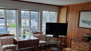 Een woonkamer met een televisie, houten meubels, een bank en uitzicht op geparkeerde auto's.