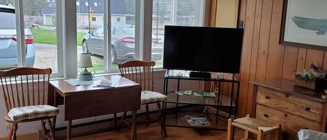 A living room with a TV, wooden furniture, a sofa, and a view of parked cars outside.