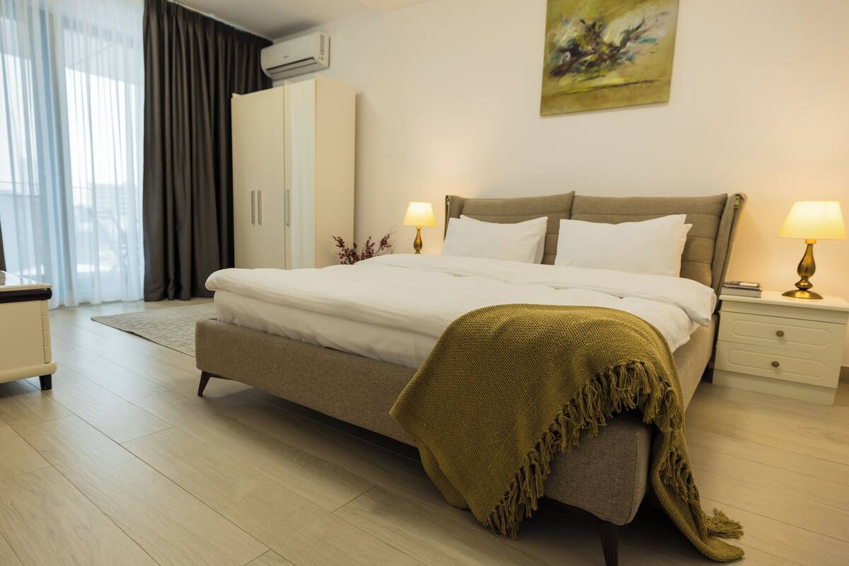 A modern bedroom with a large bed, bedside tables, a wardrobe, and a painting on the wall.