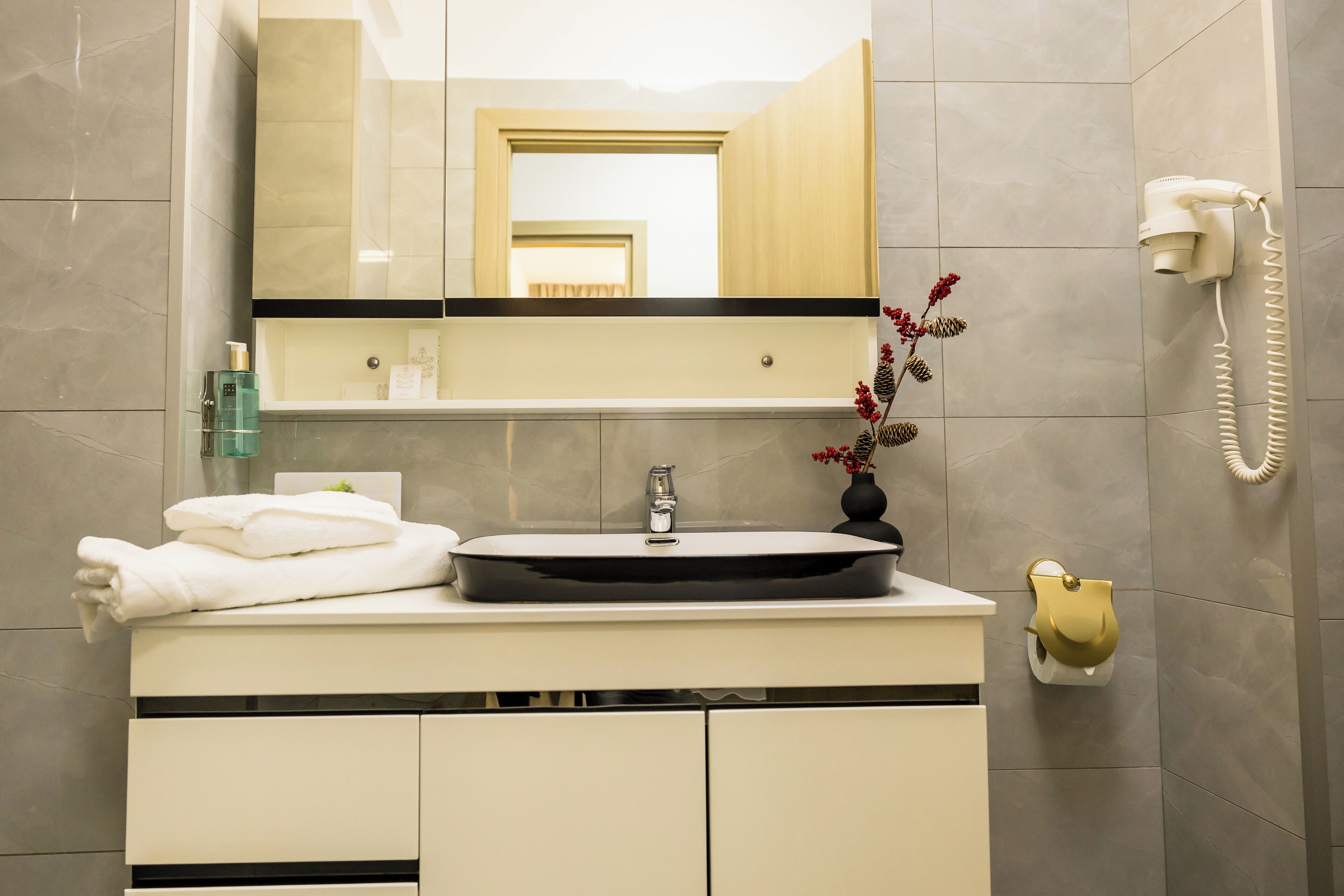 A modern bathroom with a sink, mirror, and hairdryer mounted on the wall.