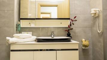 A modern bathroom with a sink, mirror, and hairdryer mounted on the wall.