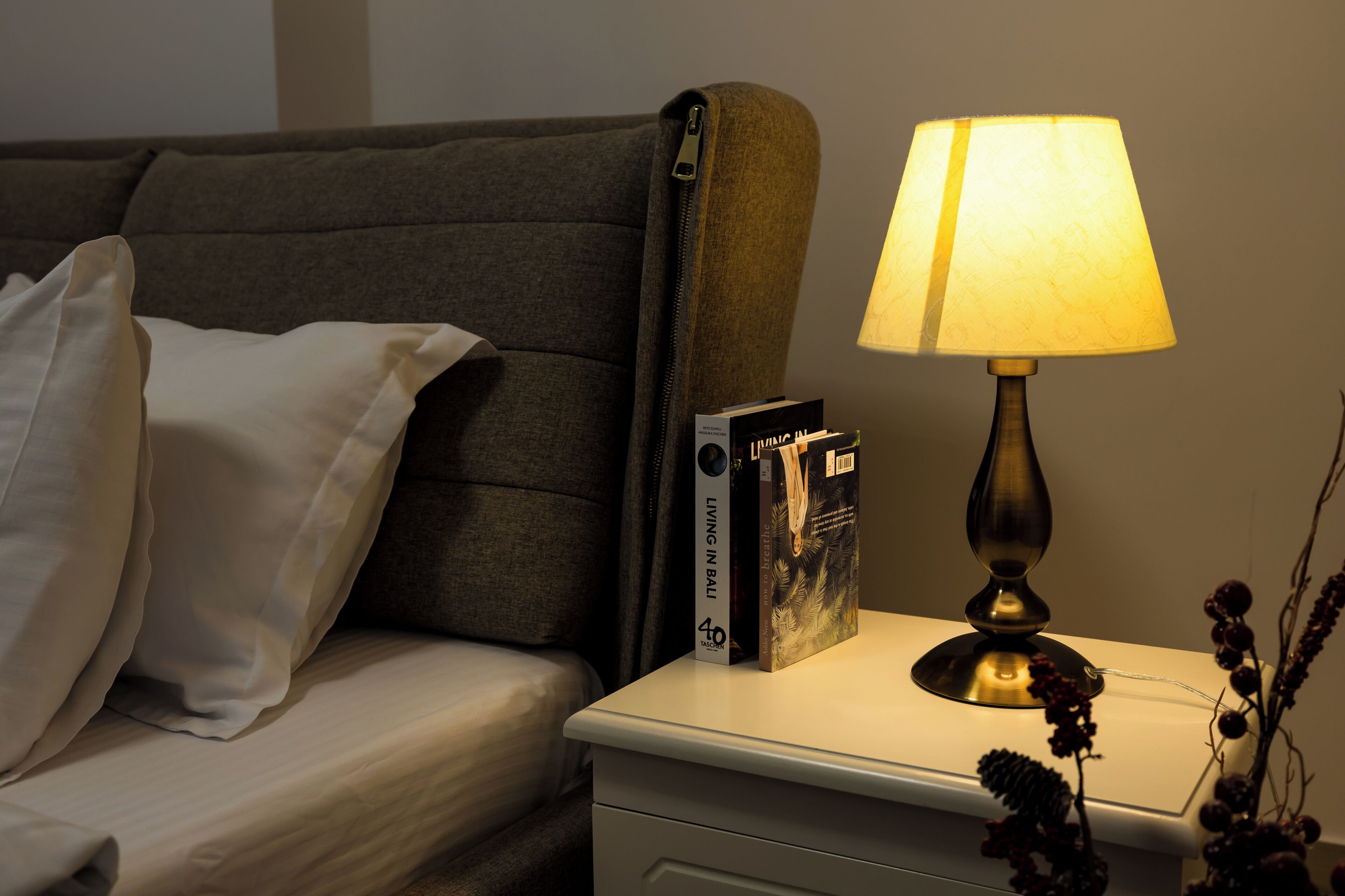 A neatly made bed with white bedding, a bedside table with a lamp, and a book titled "Living in Bali" on the table.