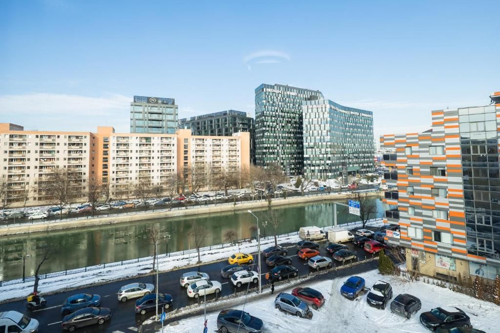 A cityscape with modern buildings, a river, and a parking lot with cars.