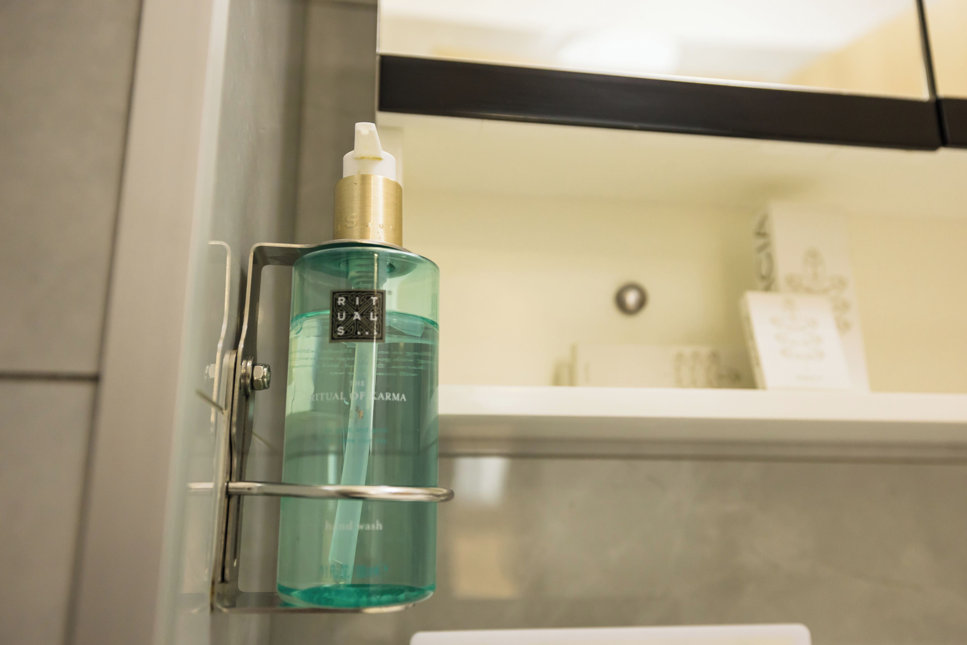 A bathroom with a sink, a mirror, and a bottle of liquid soap on a metal holder.