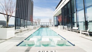 Ein Pool auf dem Dach mit einer Tiefenmarkierung von 6 Fuß, umgeben von weißen Liegestühlen und modernen Gebäuden im Hintergrund.