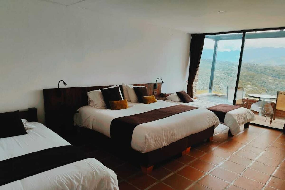 A hotel room with two beds, a large window with a city view, and a small table with chairs.