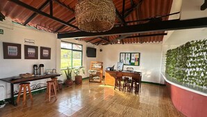 A reception area with a wooden counter, stools, a hanging light fixture, and a wall with a green lattice design. - Sierra Morena Eco-Hotel (Filandia)