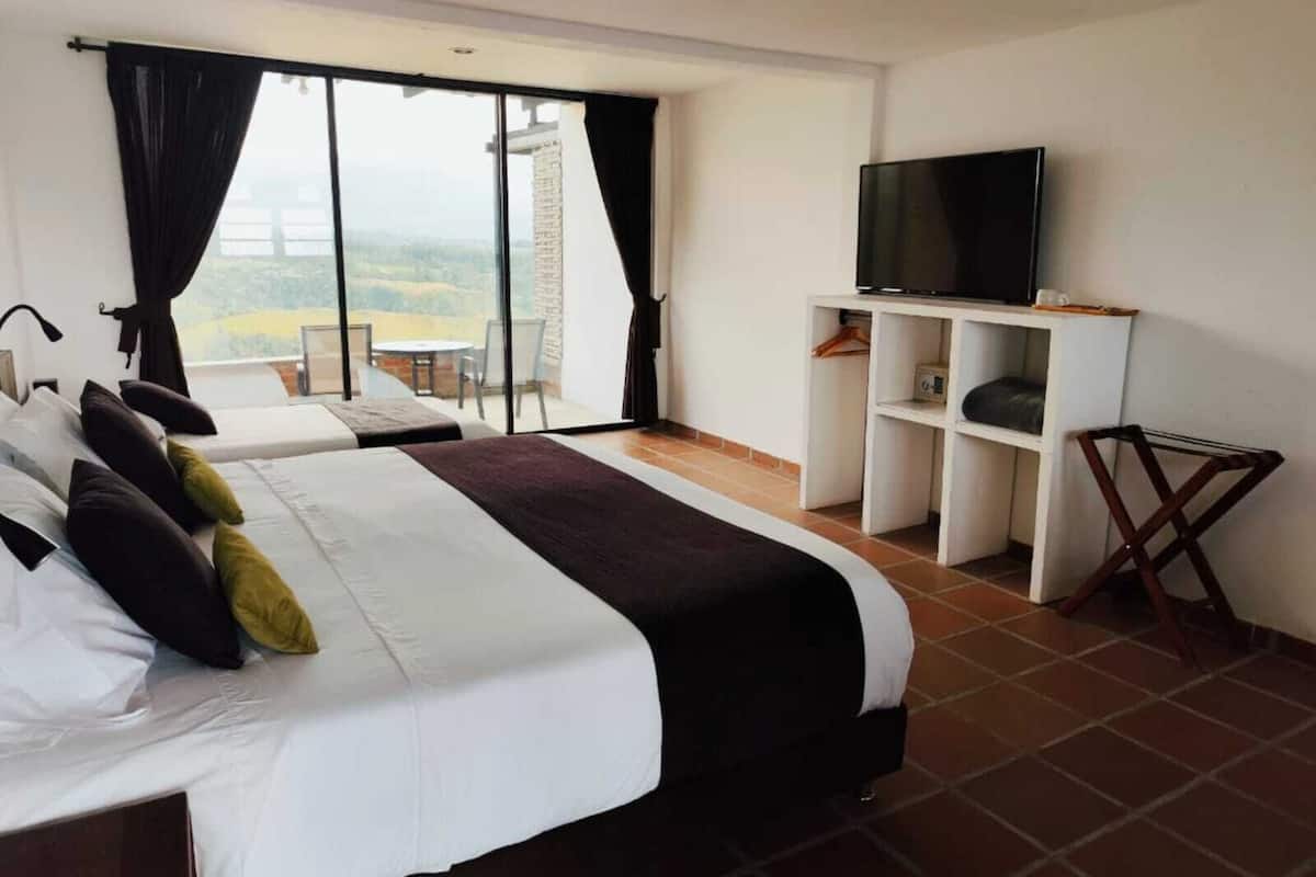 A hotel room with two beds, a TV, a balcony with a table and chairs, and a view of the countryside.