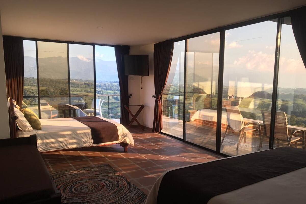 A spacious bedroom with two beds, a TV, and a balcony with a scenic view.