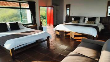 Camera d'albergo con due letti, un divano e un'ampia finestra che si affaccia su spazi verdi.