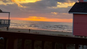 Blick auf einen Strand bei Sonnenuntergang, eine Holzterrasse und ein Gebäude mit rotem Dach.