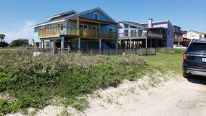 Ein Strandgrundstück mit mehrstöckigen Häusern mit Balkonen, einem Sandstrand davor und einem Feldweg, der zu einem geparkten Auto führt.